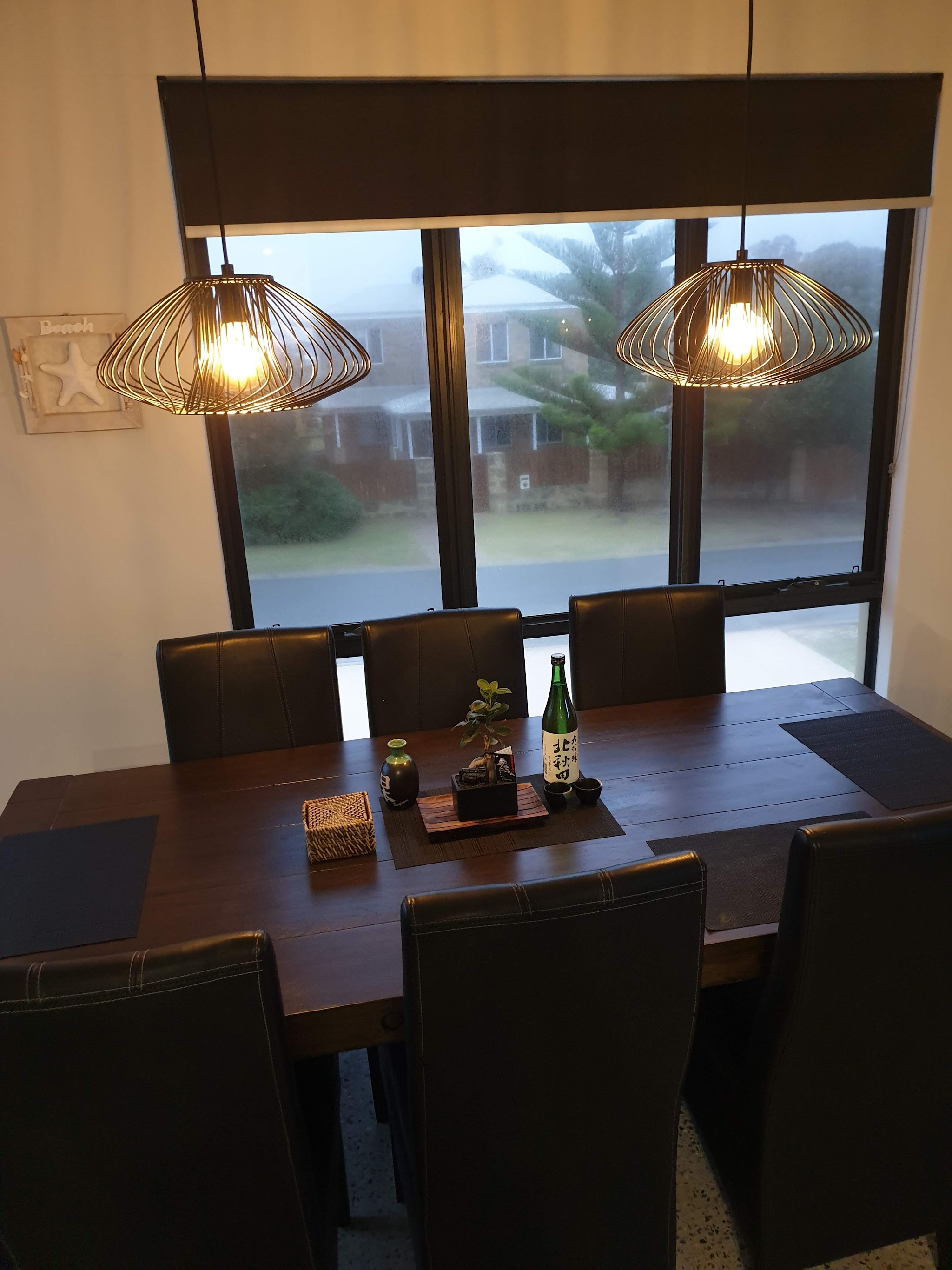 Two wire cage pendant lights lit over a timber dining table at dusk