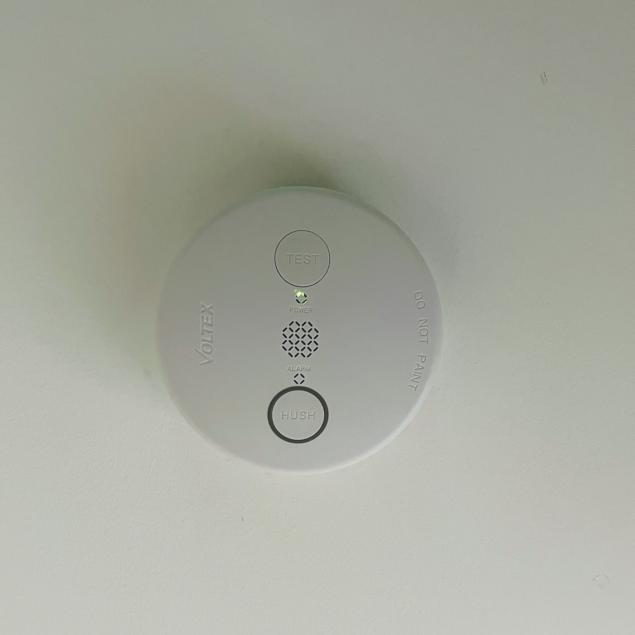 A mains powered smoke alarm fitted flush to a ceiling with its power light on
